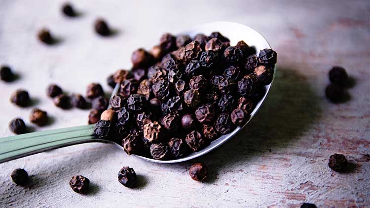 Fresh spicy peppercorns on an antique spoon placed on a wooden background.