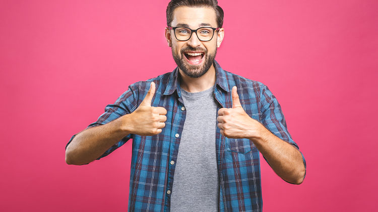 Portrait of young man in glasses showing thumbs up isolated over pink background