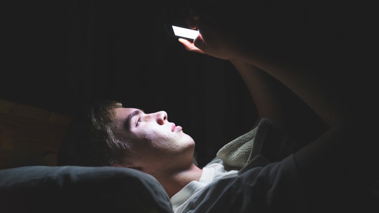 Depressed teen browsing mobile phone in dark