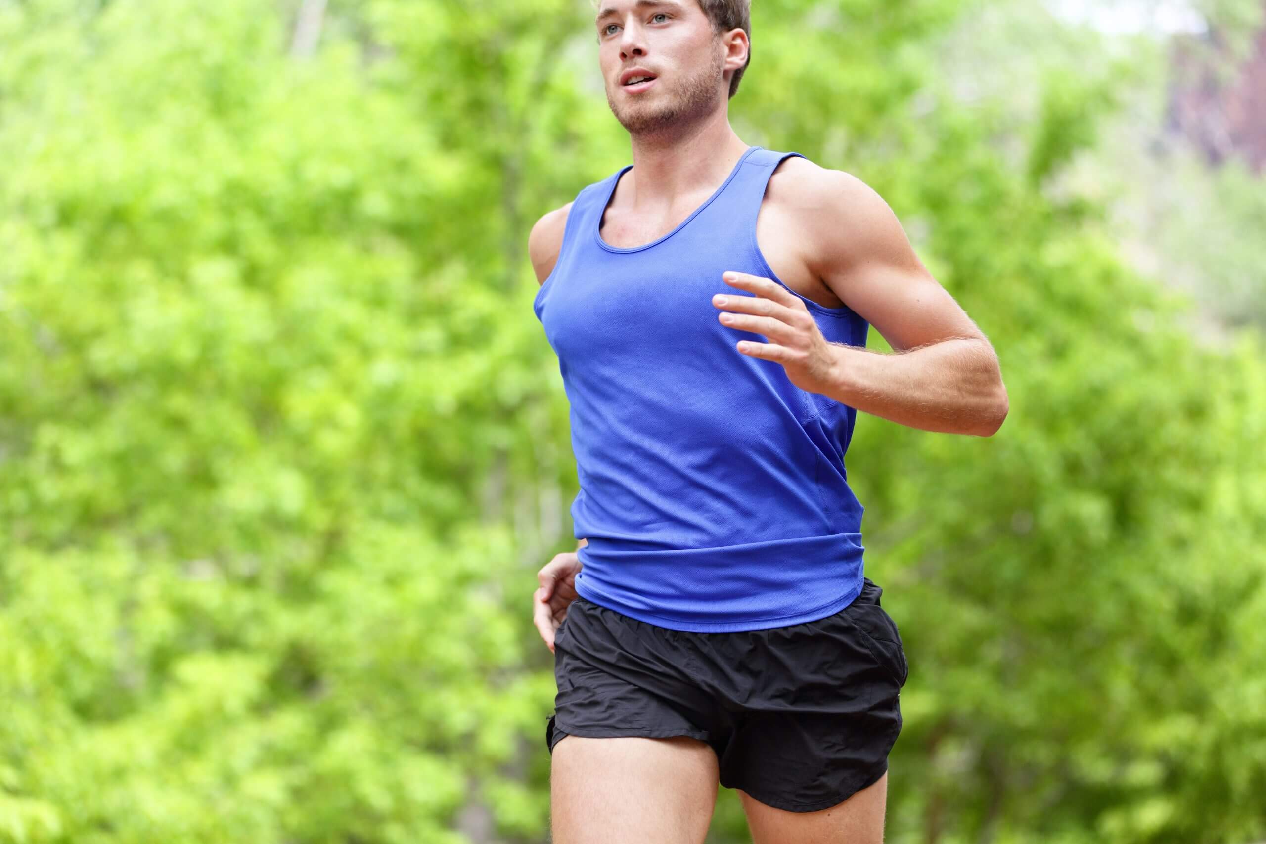 Man running on road. Sport and fitness runner training for marathon run doing high intensity interval training sprint workout outdoors in summer. Male athlete sports model fit and healthy aspirations.