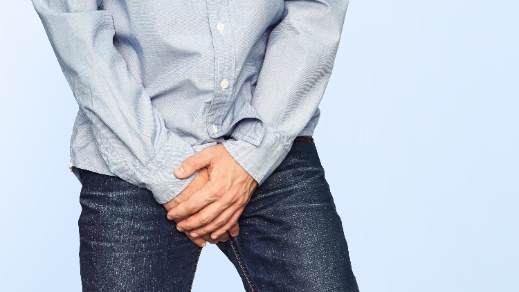 Man in blue jeans and shirt holding groin area