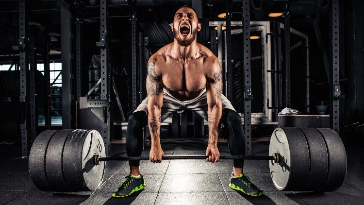 Muscular man deadlifting in dark lit gym