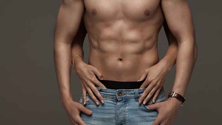 muscular naked man and female hands unbuckle his jeans on a dark background
